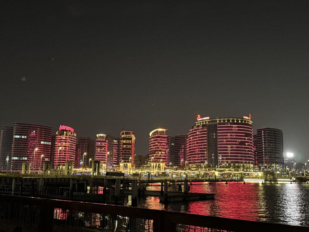 Beleuchtete Hochhäuser in Dubai Creek Harbour bei Nacht, mit Spiegelung im Wasser und leuchtenden Fassaden in Rot. Modernes Stadtbild Dubais mit luxuriöser Architektur und maritimer Atmosphäre.