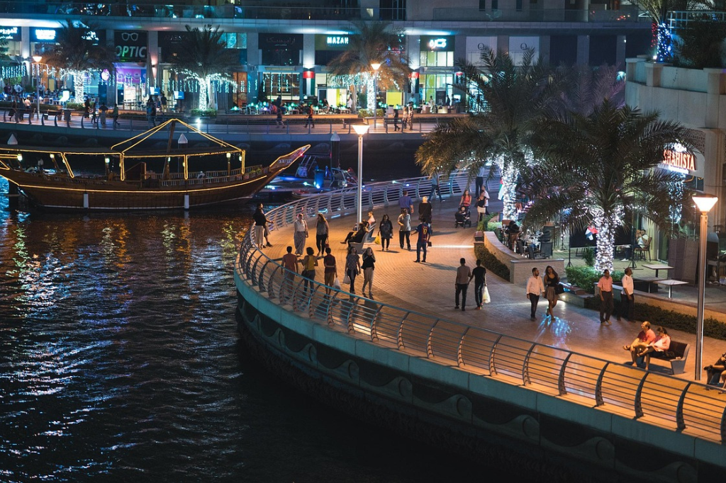Dubai Marina Waterfront bei Nacht mit Spaziergängern, Dhow-Booten und beleuchteten Geschäften perfekt für März