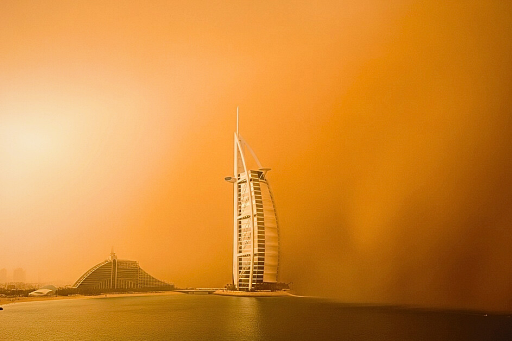 Burj Al-Arab Hotel Dubai während Sandsturm mit orange-gelber staubiger Atmosphäre und reduzierter Sichtweite